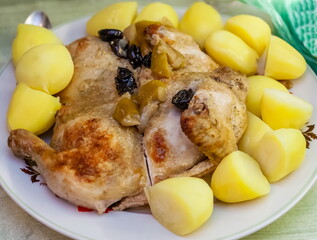 Fried chicken with prunes and boiled potatoes on a plate close-up