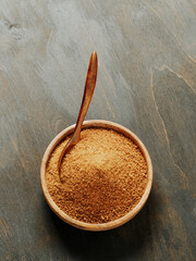 Bowl and spoon of coconut brown sugar on wooden background.Top view of full wooden bowl with raw organic coconut sugar from crystallized sap of cut flower buds coconut palm. Copy space. Vertical