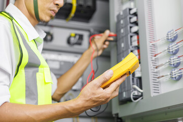 Electrical engineer or repairman holding digital multimeter to inspecting the electrical system in a factory.