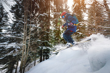 Fototapeta na wymiar A male athlete skier rides a freeride in a winter forest in the mountains. Jump against the backdrop of snow-covered trees and the setting sun