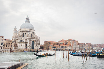 The famous Venetian gondola cruising along the Grand Canal past the basilica Santa Maria della Salute on a cloudy winter day