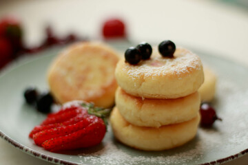 Cottage cheese pancakes (ricotta fritters) with frozen berries and yogurt on blue plate. Healthy morning breakfast or snack, dietary food. White background. Close up view. 