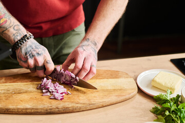 Close-up shot of unrecognizable man chopping red onion on wooden cutting board with knife