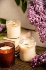Cozy home decor. Burning aroma candles on the background of wooden textures.Composition with eco candles and a bouquet of spring lilac.Aromatherapy and relaxation.