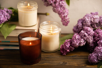 Obraz na płótnie Canvas Cozy home decor. Burning aroma candles on the background of wooden textures.Composition with eco candles and a bouquet of spring lilac.Aromatherapy and relaxation.