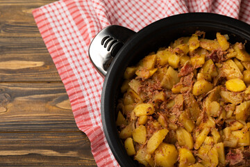 Braised pork with potatoes and onions on a brown textured wood. Copy space. Place for text. Fried potato recipe.