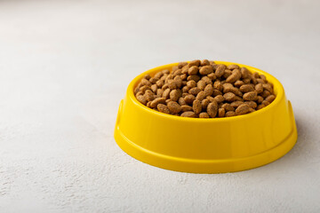 Dry cat food in a yellow bowl on a cement background. Vitamins and nutrients for good health and energy of pets.Copy space.