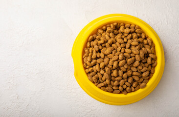 Dry cat food in a yellow bowl on a cement background. Vitamins and nutrients for good health and energy of pets.Copy space.