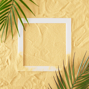 Top view of green tropical leaves and white frame on sand color background. Flat lay. Minimal summer concept.