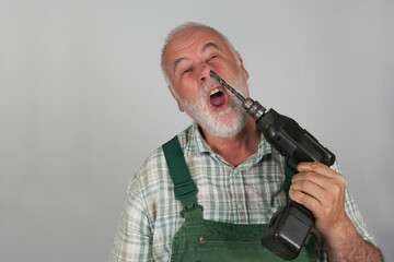 Taken literally in the nose picking. An old craftsman picks in his nose with his drilling machine, in front of a white wall.  Danger! Nose picking can cause injuries.