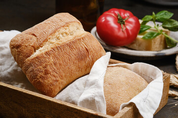 Italian ciabatta bread or bun in a wooden box with white kitchen towel. Freshly baked traditional bread and tomato. Homemade rustic  bread or Italian Ciabatta. Shallow depth of field