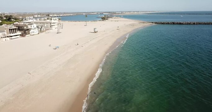aerial footage of the silky brown sand and vast blue ocean water at the beach with people relaxing in the sand and homes and apartments along the beach at Seal Beach in Seal Beach California USA