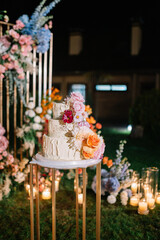 Beautiful white four tier cake with fresh flowers with fairly light and lanterns glowing in the background.