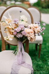Wedding bouquet with white flowers, roses, greens and ribbons on the chair. Outdoor wedding