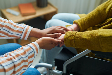 Close-up of caregiver holding hands with senior woman in wheelchair, she giving her support