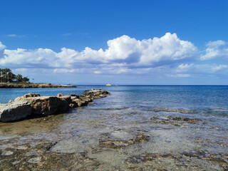 Fototapeta na wymiar A stone ridge, long-hardened lava, the shore of the Mediterranean Sea against the backdrop of the sea with a pleasure boat and a blue sky with clouds.