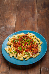 Large plate of bolognese pasta with green onions on a wooden table.