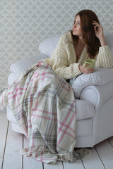 Young woman with blanket holding a cup of tea in armchair