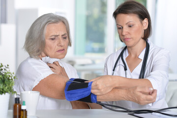 Female doctor measures the pressure her senior patient