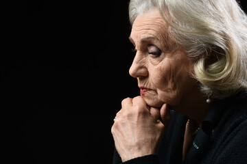 Beautiful sad elderly woman with gray hair on a dark background