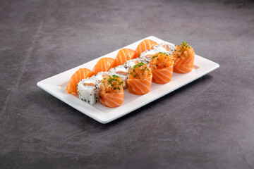 Fresh made sushi mix. Different kinks of salmon sushi served on white plate. Studio shoot on slated background.