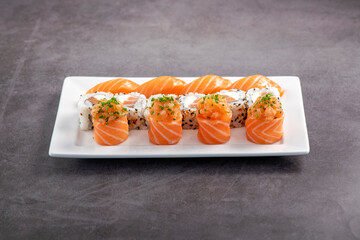 Fresh made sushi mix. Different kinks of salmon sushi served on white plate. Studio shoot on slated background.