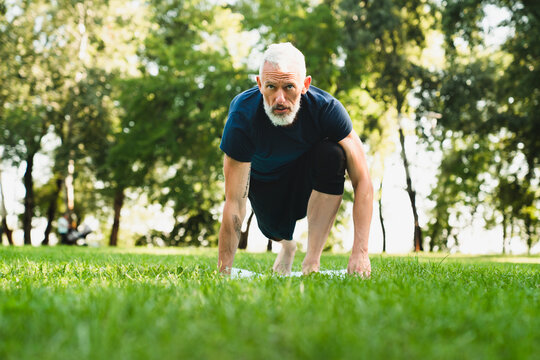 Stretching Yoga Exercises On Fitness Mat Outdoors In Public Park. Active Seniors Concept. Caucasian Mature Man Doing Workout Outside.