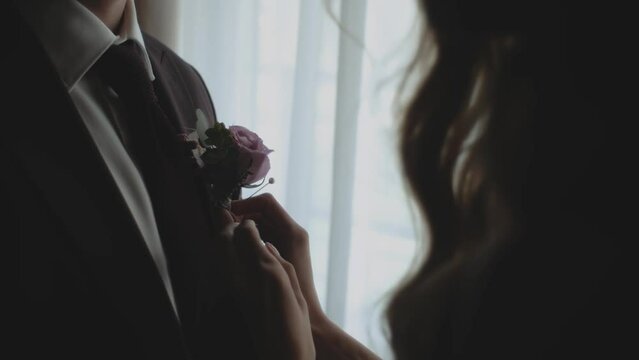 Silhouette of newlywed, loving couple standing near the window close-up. Bride touches a boutonniere the groom and sit on a bench in the old house