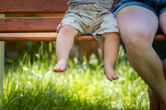 Baby grow up concept: Close up of barefoot baby feet sitting on park bench, summer time