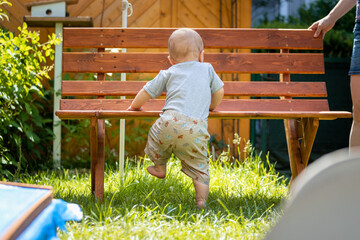 Baby grow up concept: Close up of toddler baby standing on park bench, summer time