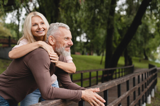 Happy relaxed caucasian mature couple spouses husband and wife hugging embracing together while walking in park on romantic date.