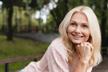 Cheerful caucasian mature blonde woman wife with toothy smile relaxing resting walking in city park...