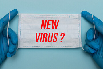 Hands in blue medical gloves hold a protective medical mask with the red inscription NEW VIRUS?...