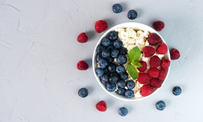 A bowl with cottage cheese, fresh raspberry and blueberry. Delicious and healthy dessert. Сlose-up. Top view. Place for text.