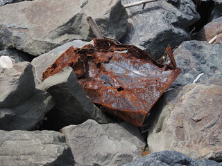 Textures of the beach with rocks and rusty metal pieces strewn along the shore