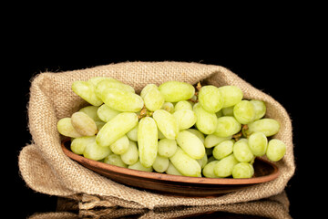 One bunch of white seedless grapes with a jute bag, close-up, isolated on a black background.