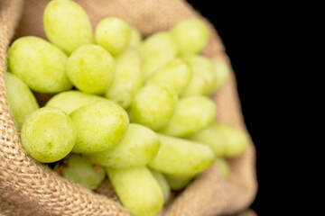 One bunch of white seedless grapes with a jute bag, close-up, isolated on a black background.