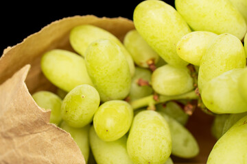 One bunch of white seedless grapes with a paper bag, close-up, isolated on a black background.