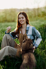 Happy woman sitting in nature and playing with her pet in the park sitting on the green grass 