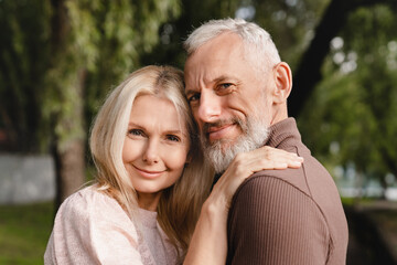 Fototapeta premium Confident happy cheerful mature couple embracing hugging each other looking at the camera with love and passion. Protection and trust concept.