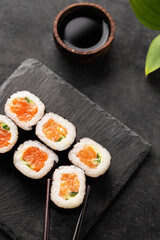 The concept of sushi maki with salmon, cucumber and nori on black slate boards with soy sauce. Traditional Japanese food. Top view