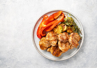 Grilled pork dish with fresh vegetables pepper and zucchini with spices in a plate on a blue background. Top view and copy space