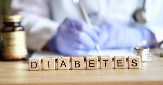 Doctor endocrinologist writing out prescription on background of wooden cubes with word diabetes closeup 4k movie