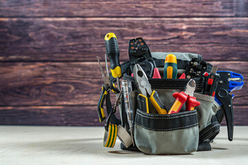 Electrician's bag with a professional electric tools. Dark wood background. Front view. Place fot text.