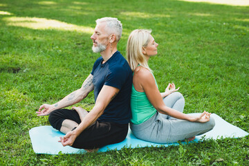 Caucasian mature couple meditating together, feeling zen like outdoors. Fitness trainer coach sitting in lotus position with mature woman in park - Powered by Adobe