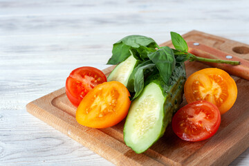 cucumber, yellow and red tomato, basil and knife lie on a wooden board, healthy food concept, vegetable diet