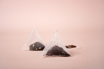 two triangular tea bags stand on a beige background, close-up