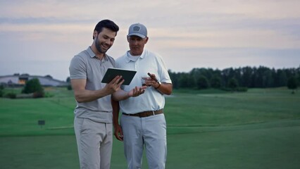 Two golfers search tablet on field landscape. Happy men chatting online outside.