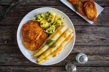 Fried schnitzel and white boiled asparagus with potato served on wooden table
