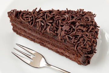 Slice of chocolate cake with cream filling and chocolate shavings next to fork from above.